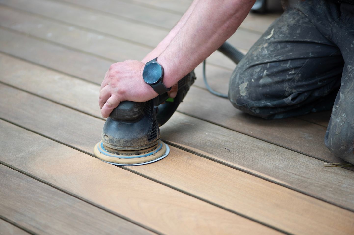 Carpenter sanding a wooden deck during resurfacing